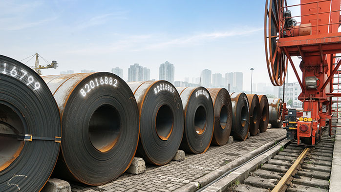 A striking industrial scene, where large steel sheet rolls on tracks against a backdrop of towering city skyline demonstrate the impact of section 232 tariffs on steel industry