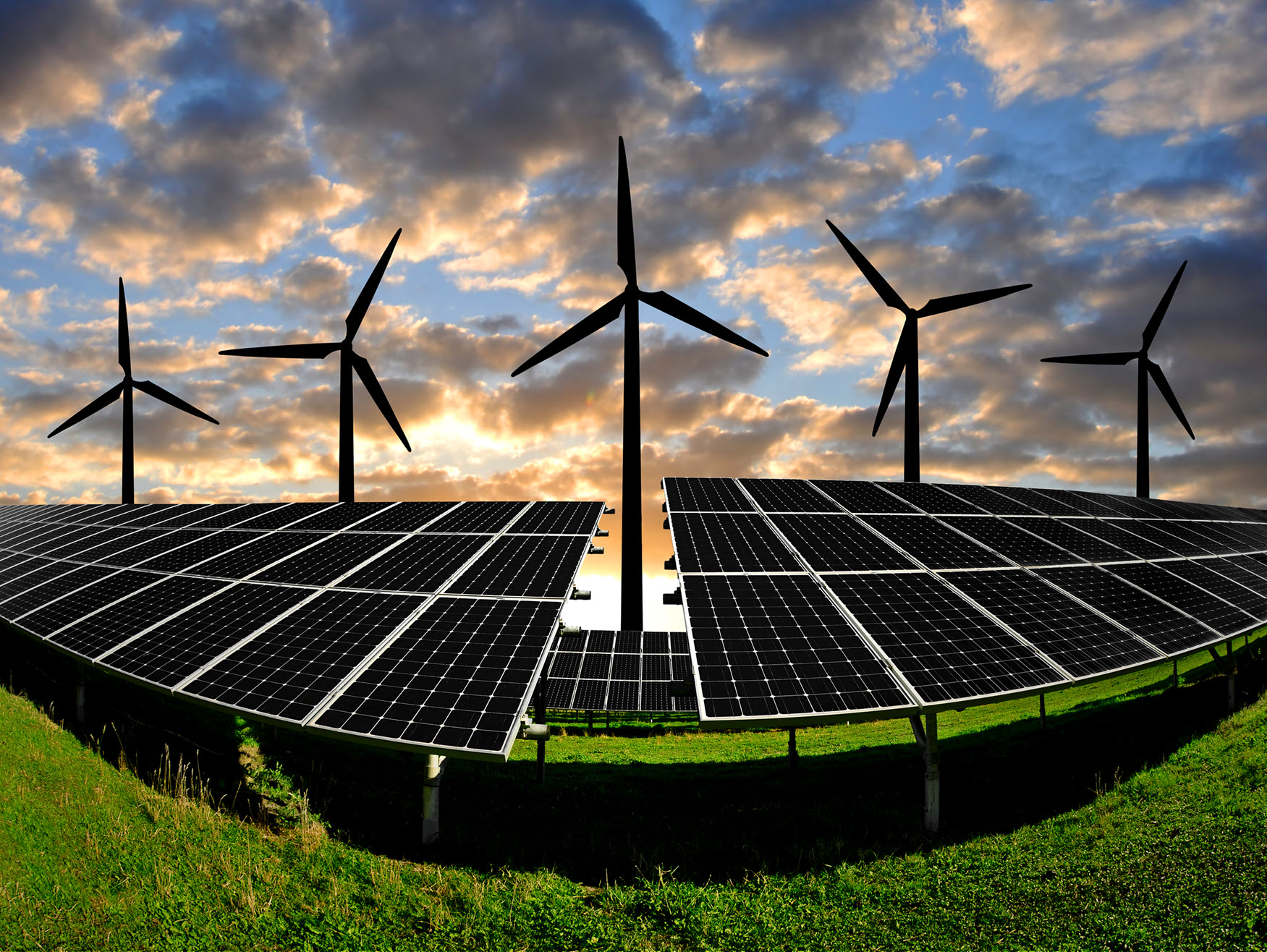 Wind turbines and solar panels, for decarbonising electricity, are shown on a field, with a cloudy sky at sunset 